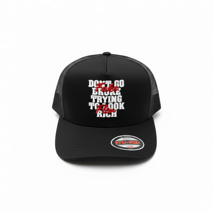 Black MUKA Fake Flex trucker hat with mesh back and curved brim, featuring the brand logo on the front panel.